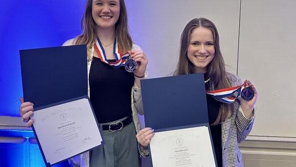 2 smiling students holding award medals and certificates